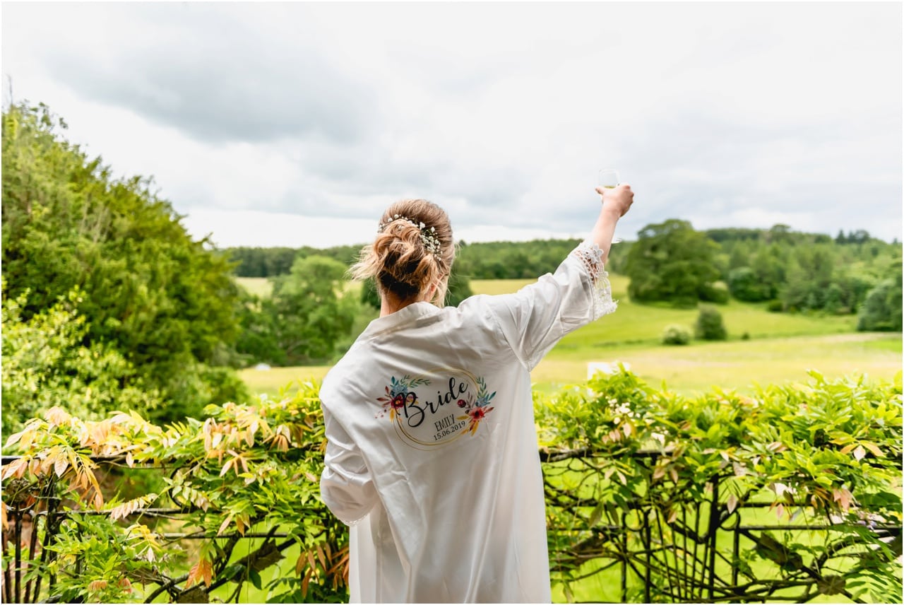 Bride raises a glass to guests from a balcony of the bridal suite in her personalised dressing gown.