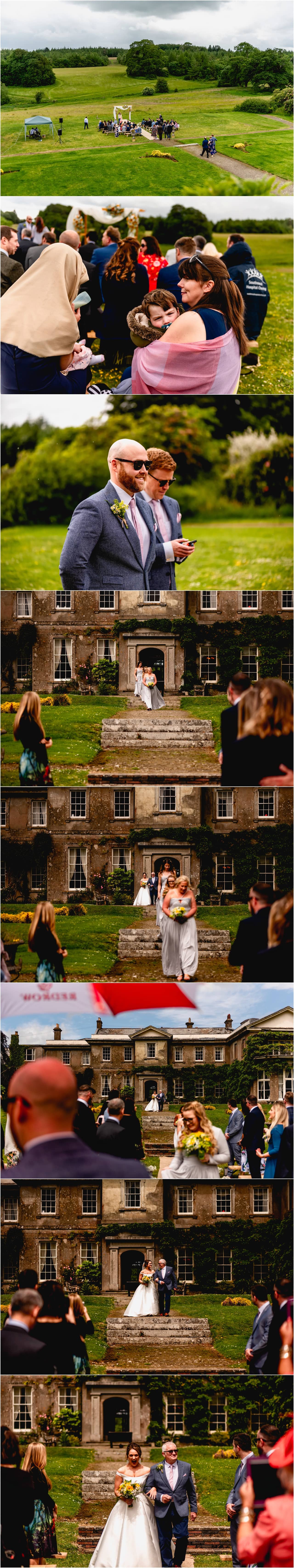 Entrance of the bride in the gardens of Buckland House in Devon, bride walks down garden steps with Dad to greet groom.