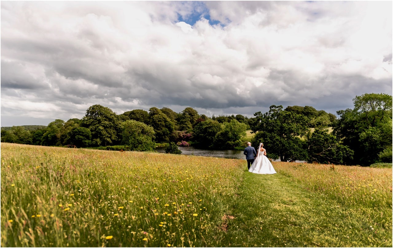 Bride and groom walk away from camera through fields in Devon.