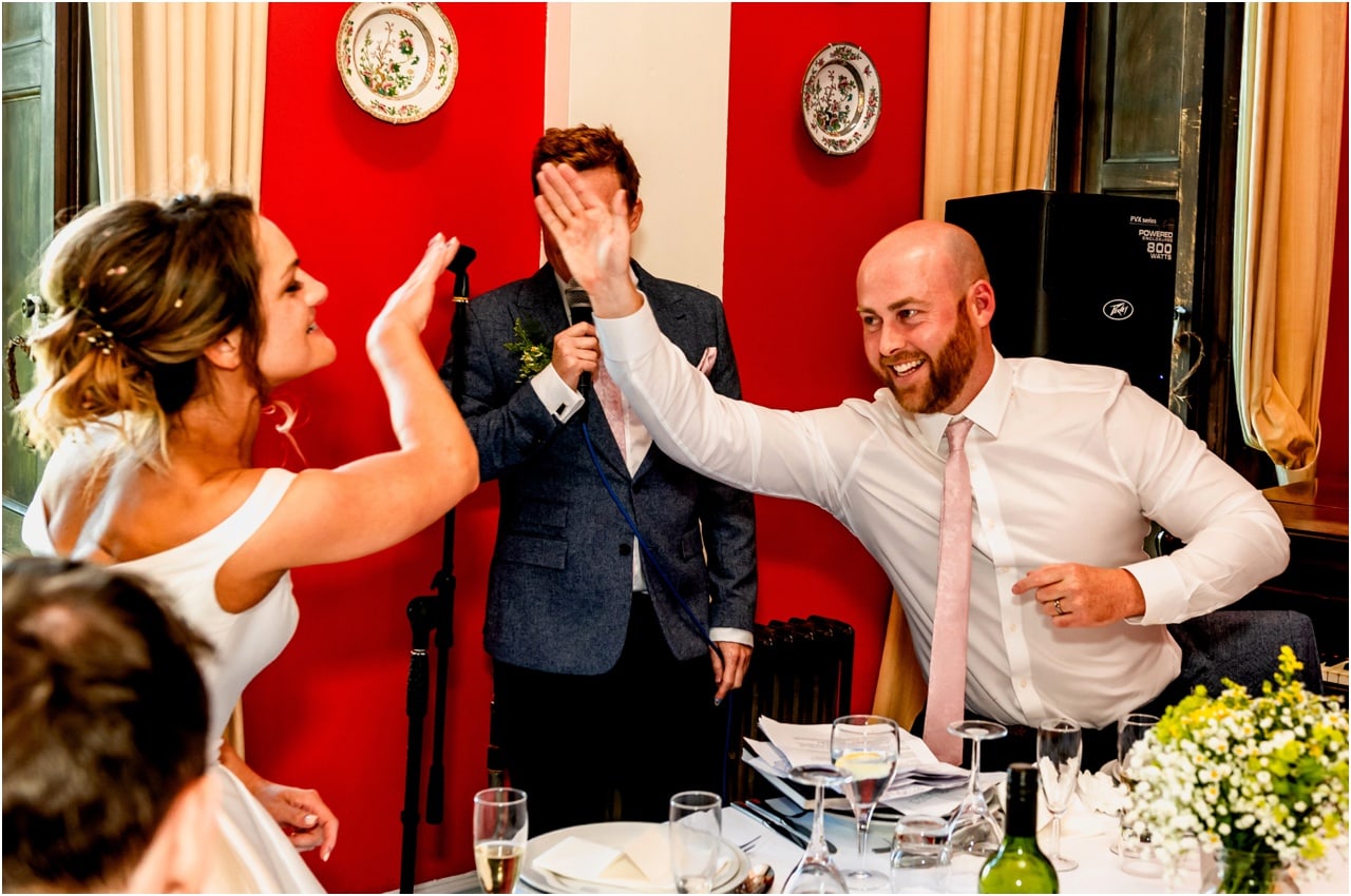 Bride and groom high five during wedding speeches.