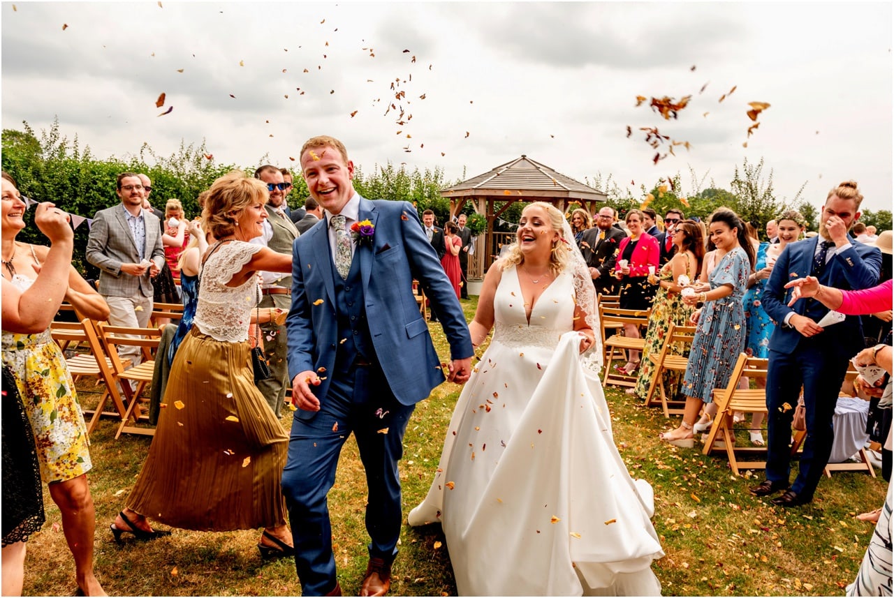 Bride and groom walk down aisle through shower of confetti after wedding ceremony.