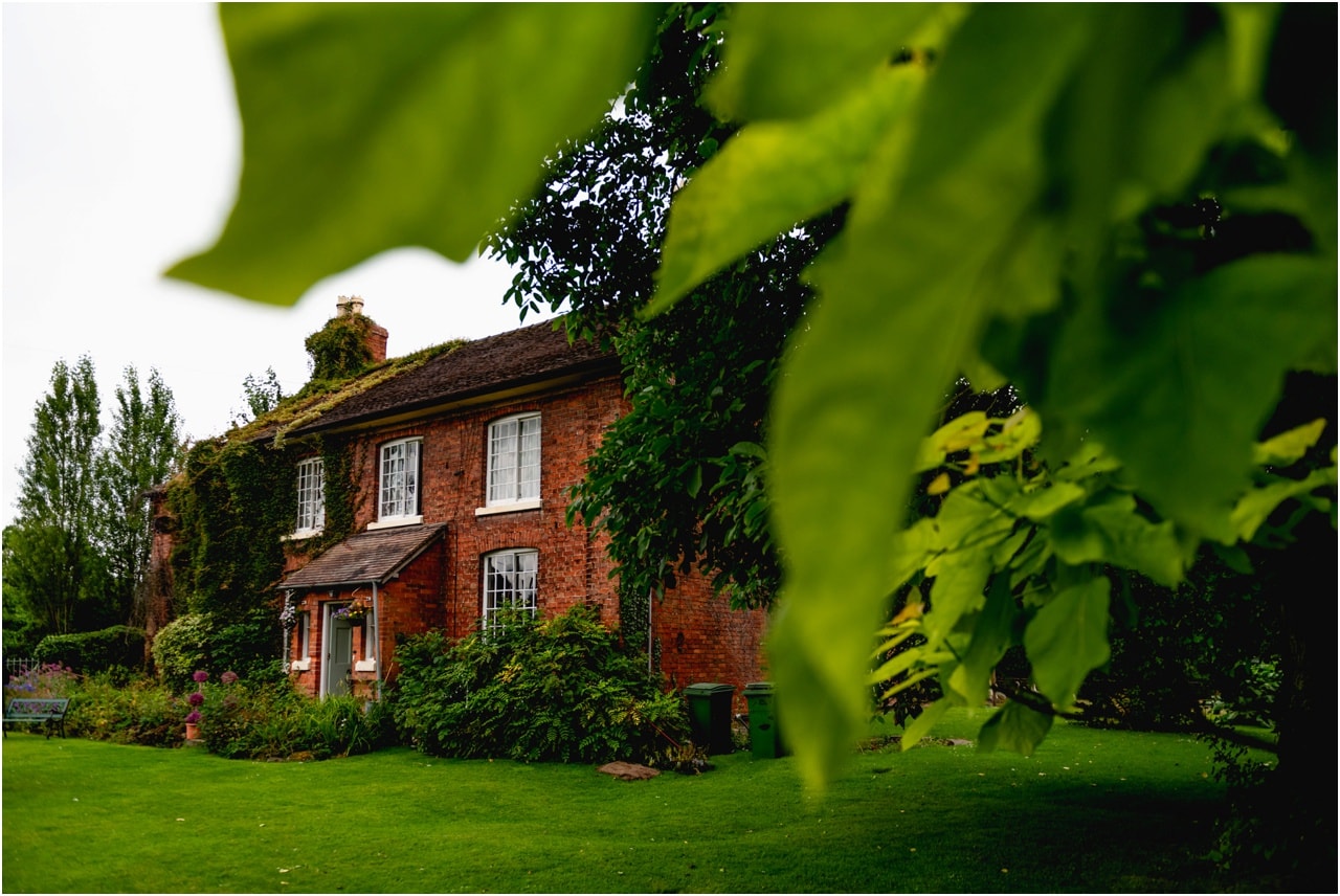 Exterior view of a cottage taken through green leaves