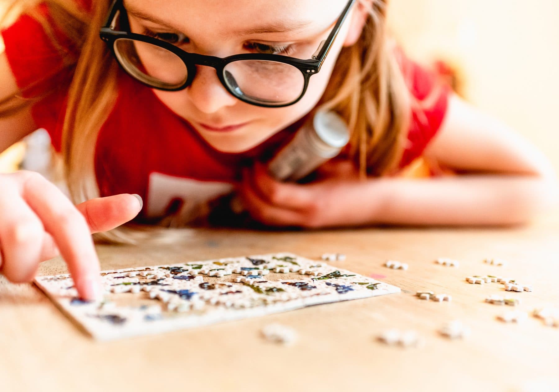 blonde haired girl in glasses doing miniature jigsaw during lockdown and self isolation for Covid 19 Coronavirus