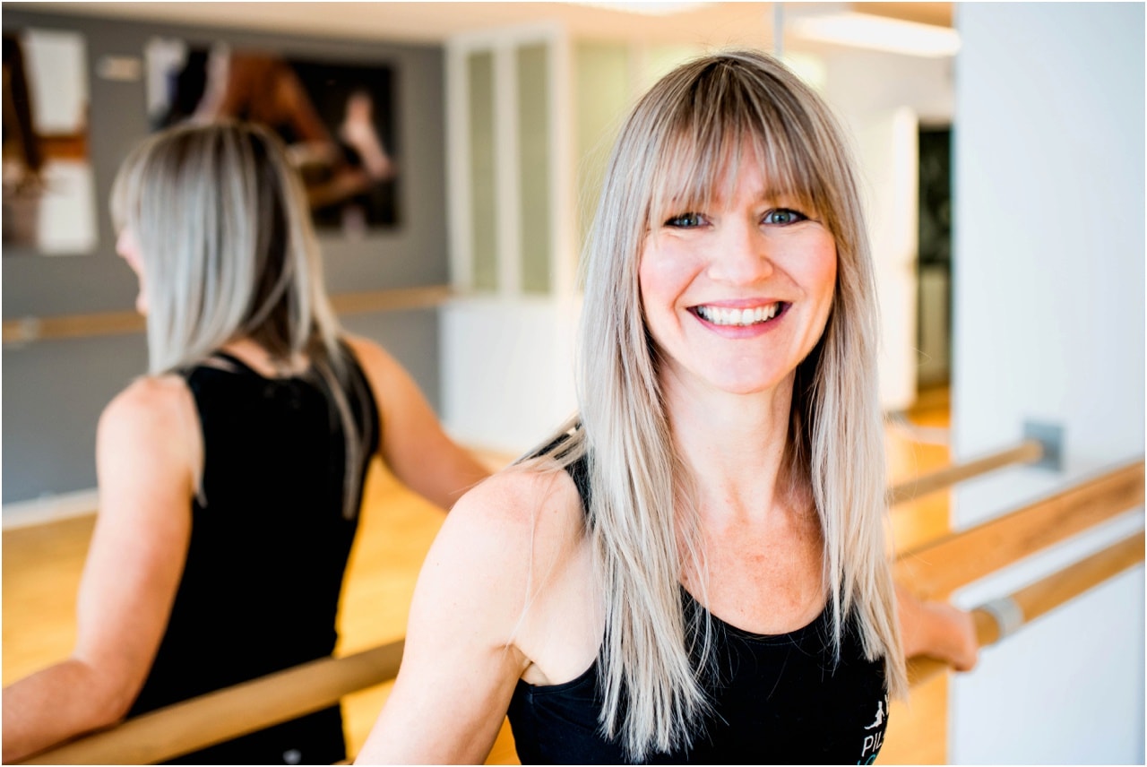 Pilates Lounge Owner and instructor reclines against ballet bar in barre studio in Sutton Coldfield.