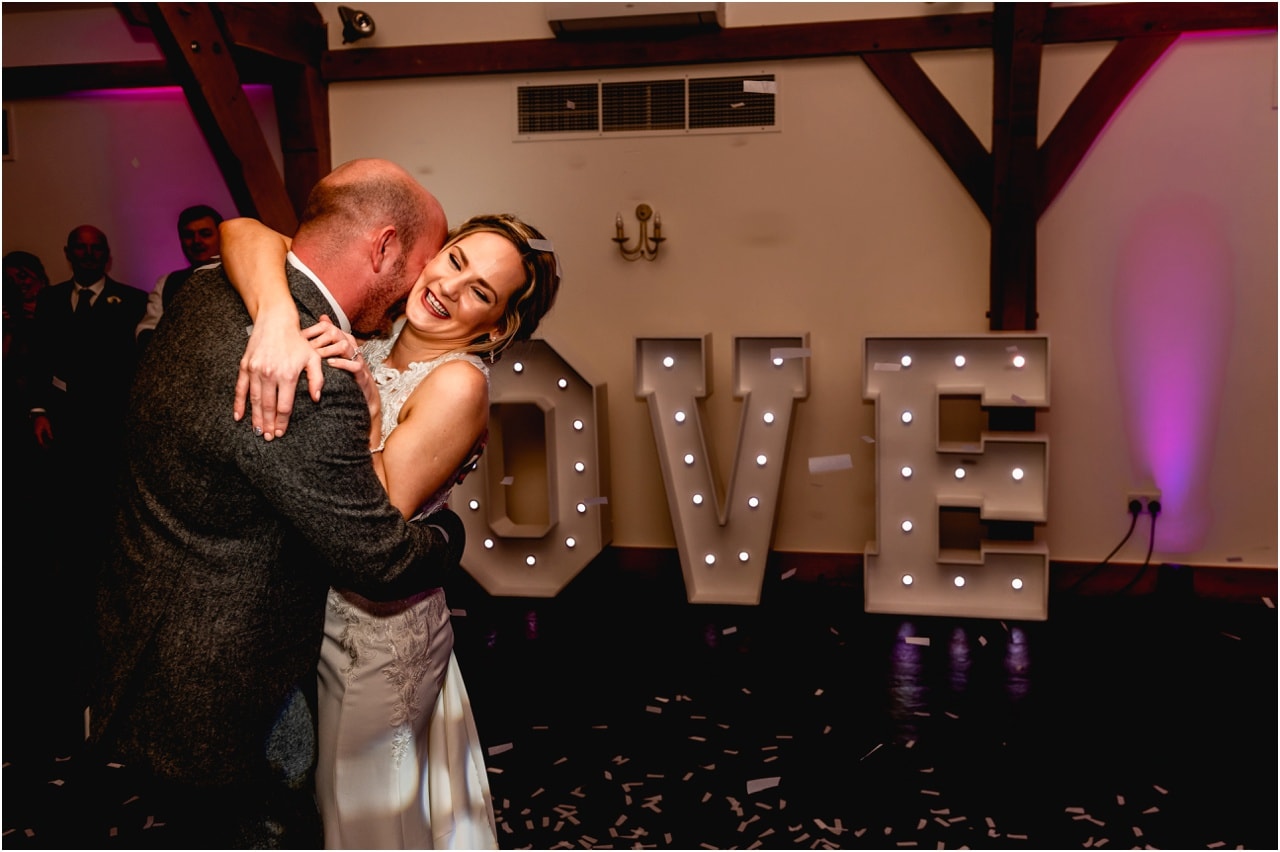 Bride and groom have their first dance at a wedding with lit up LOVE letters behind them.