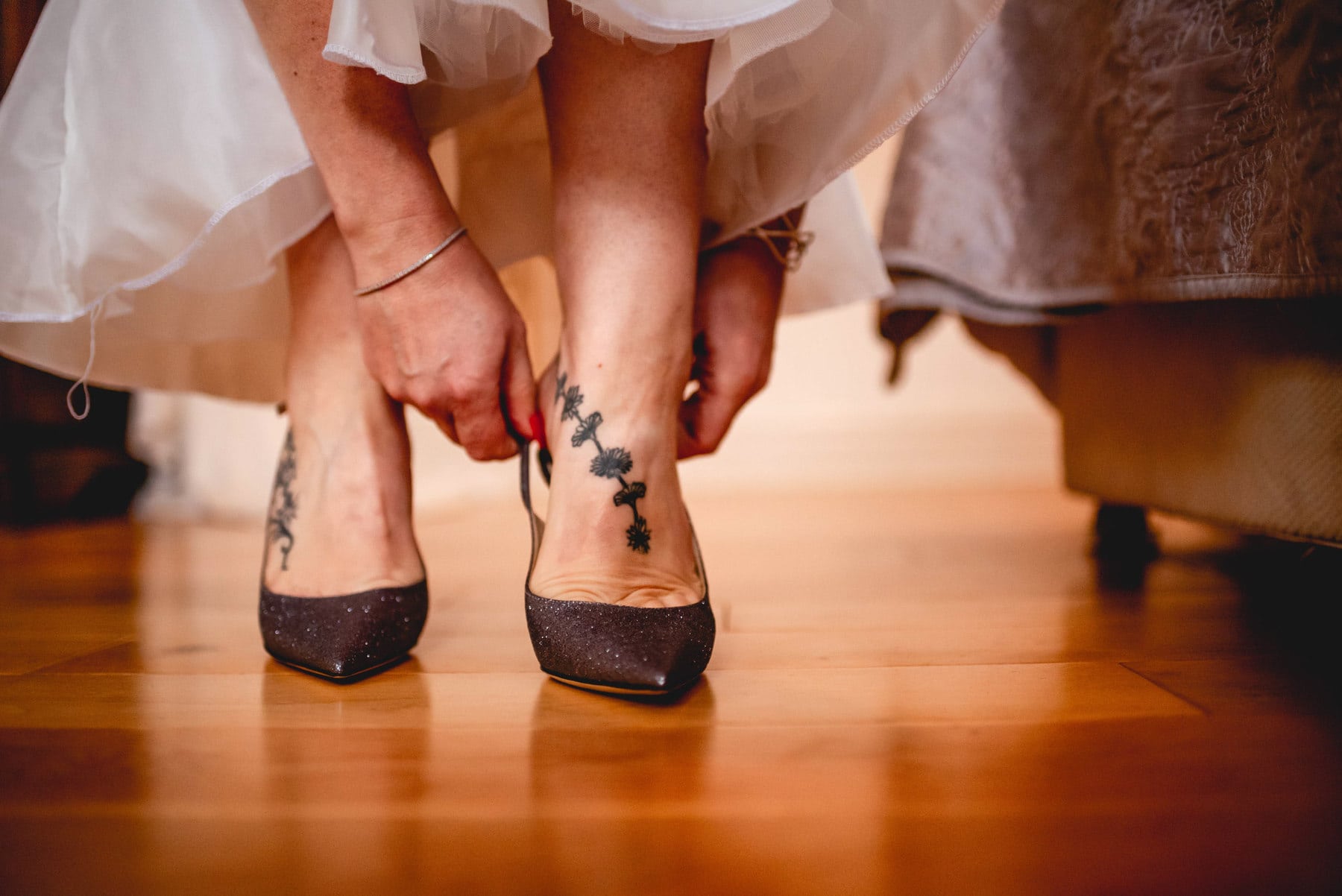 Hands help to shuffle tattooed feet into sparkly grey Jimmy Choo stiletto shoes