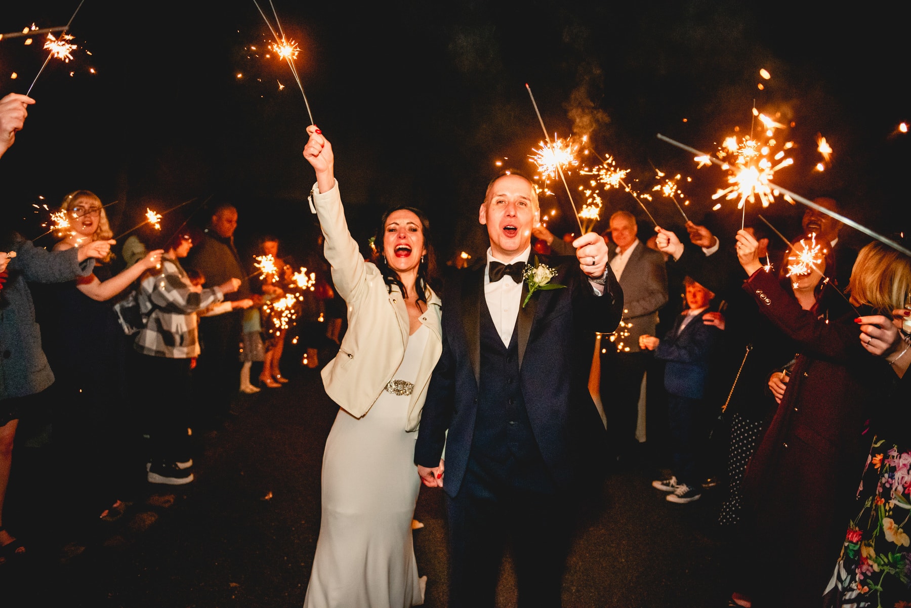 Sparkler exit at a barn wedding venue, couple hold their sparklers in the air shouting with joy while guests wave them through the tunnel of people. Best Wedding Photography of 2021