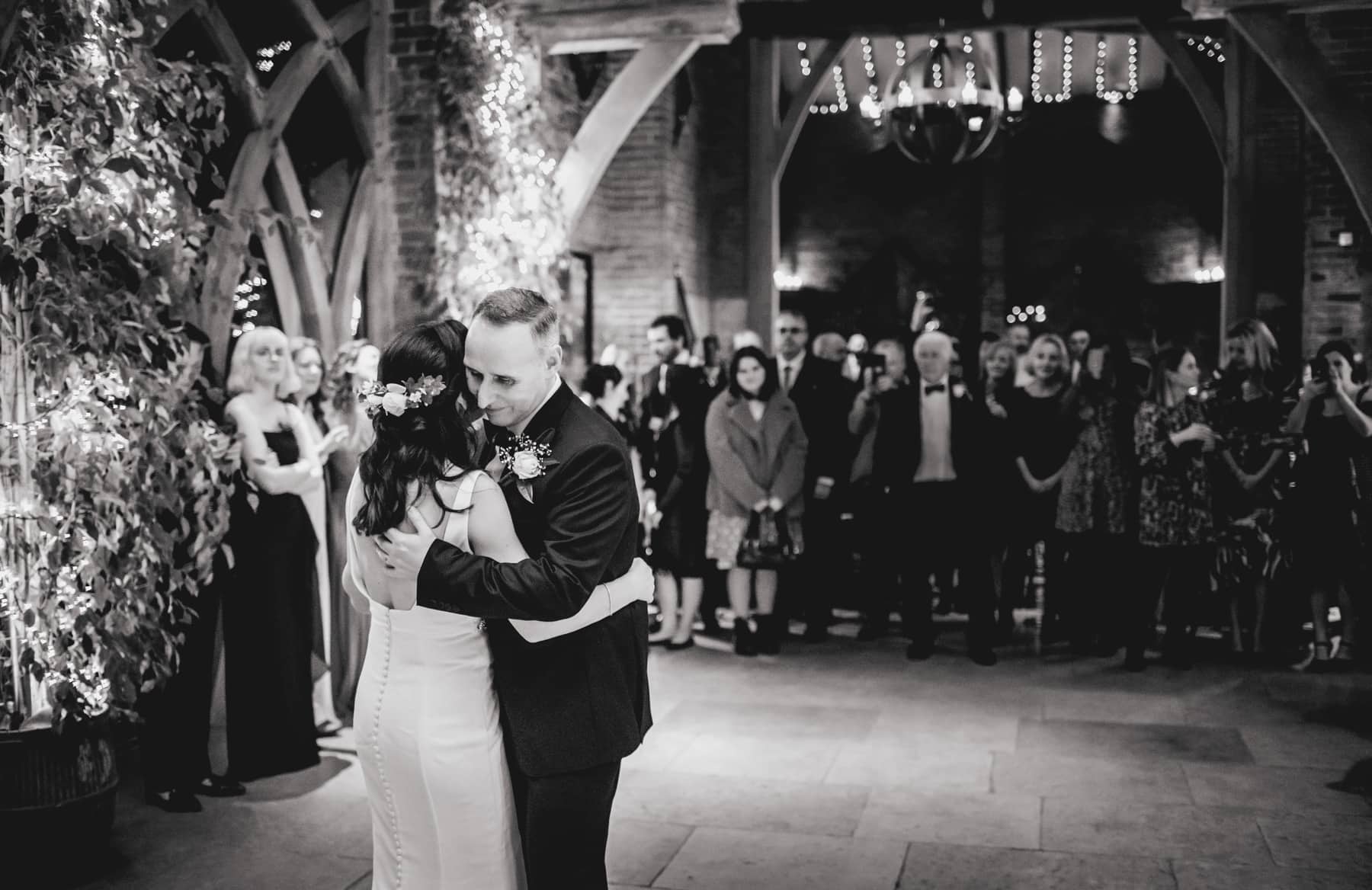 Black and white photo of bride and groom taking their first dance in a barn