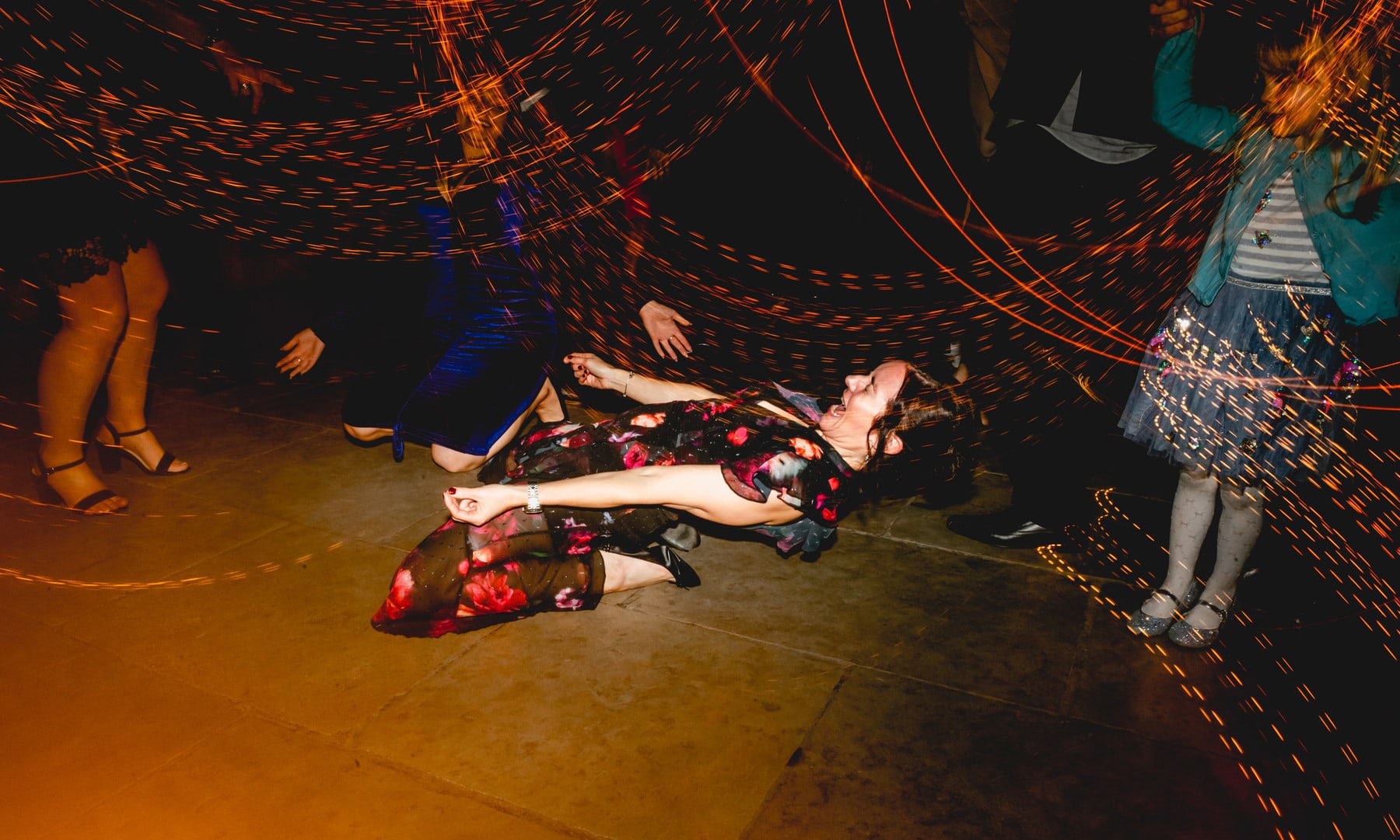 Lady lies on the floor wearing a flowery dress doing the limbo while onlookers watch. Best Wedding Photography of 2021