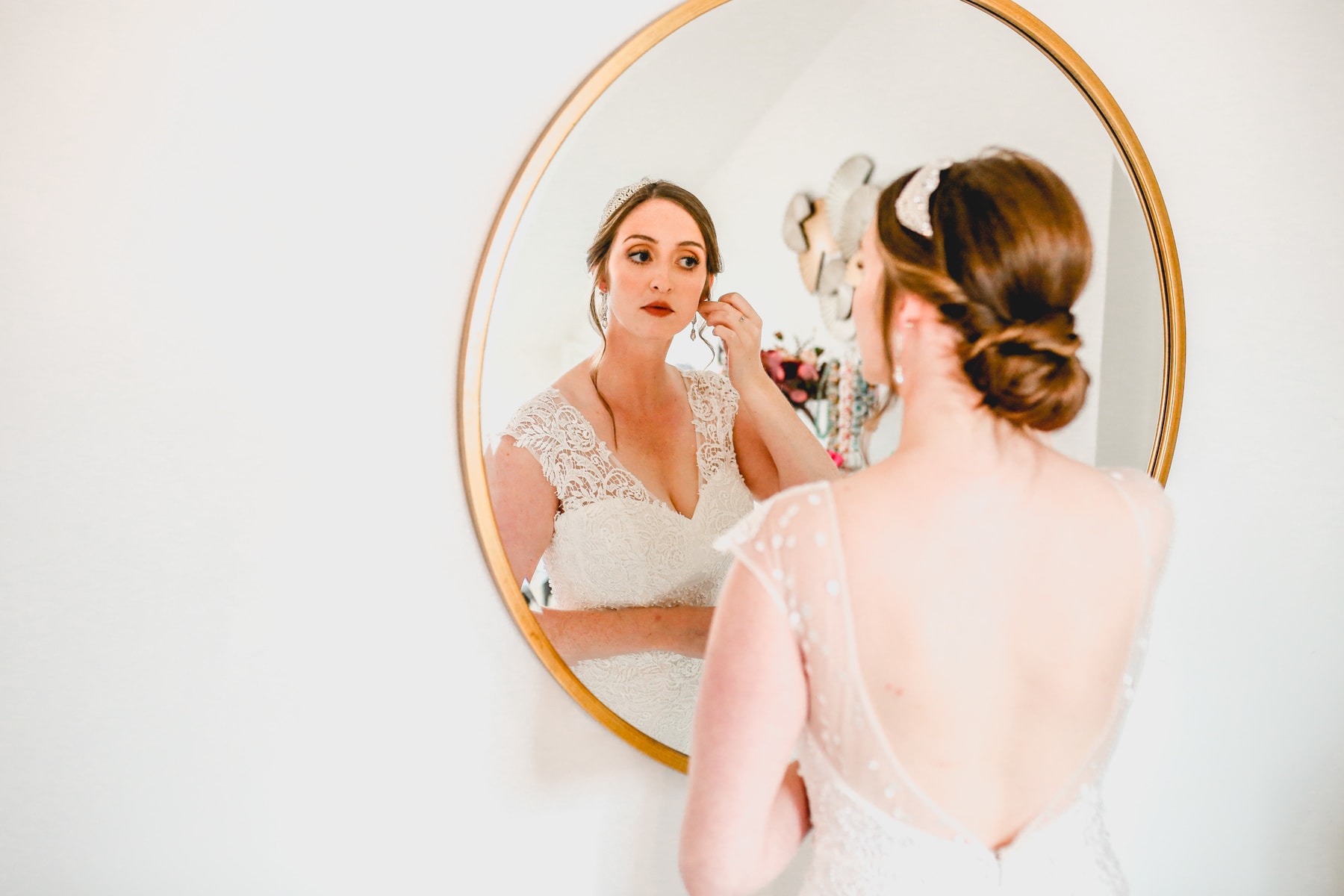 Bride looks at her reflection in a round mirror dusting her earrings