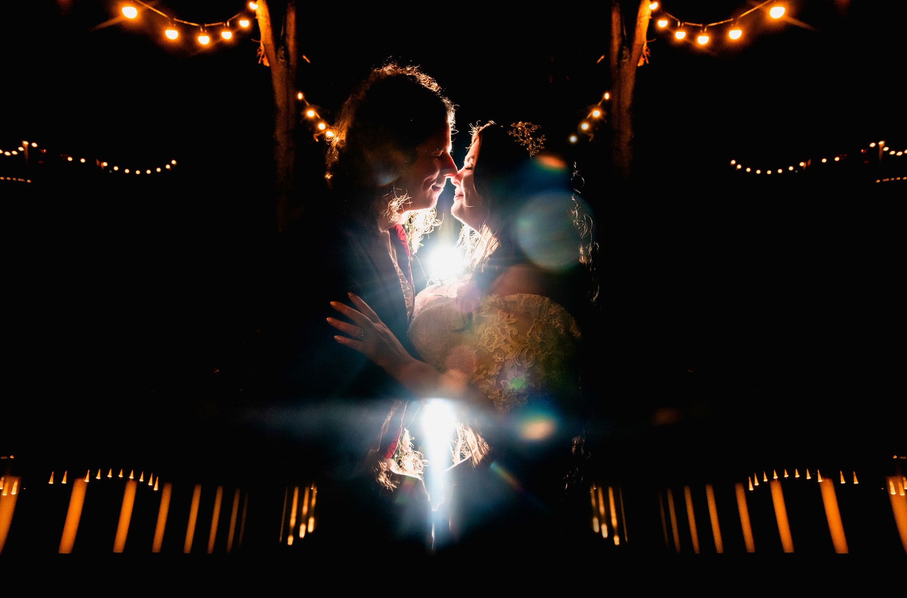 Creative portrait of couple looking at each other surrounded by lights outside at night . Lit from behind with a reflection of their heads.
