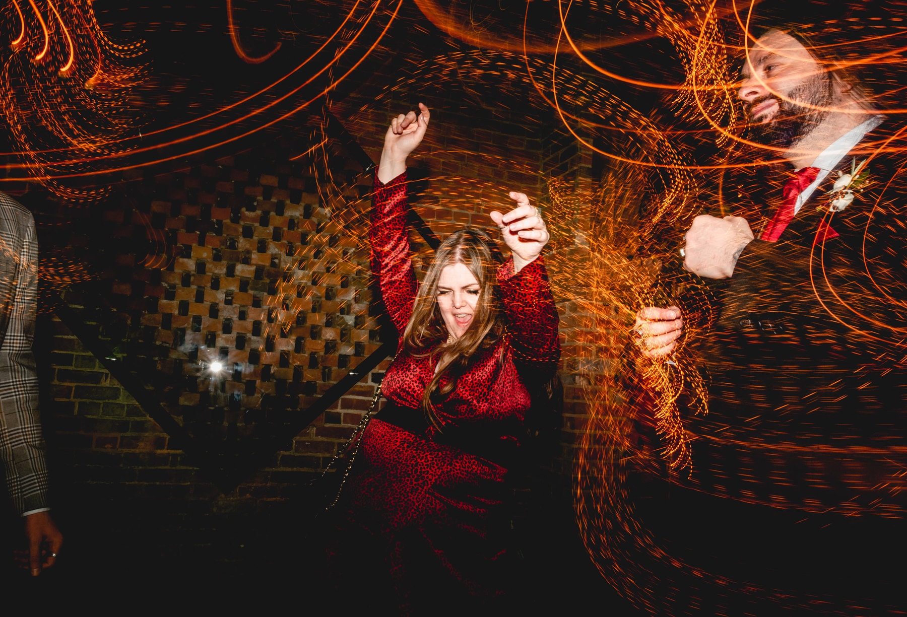 Guest dances at a wedding wearing red dress with her hands in the air surrounded by light trails. Best Wedding Photography of 2021