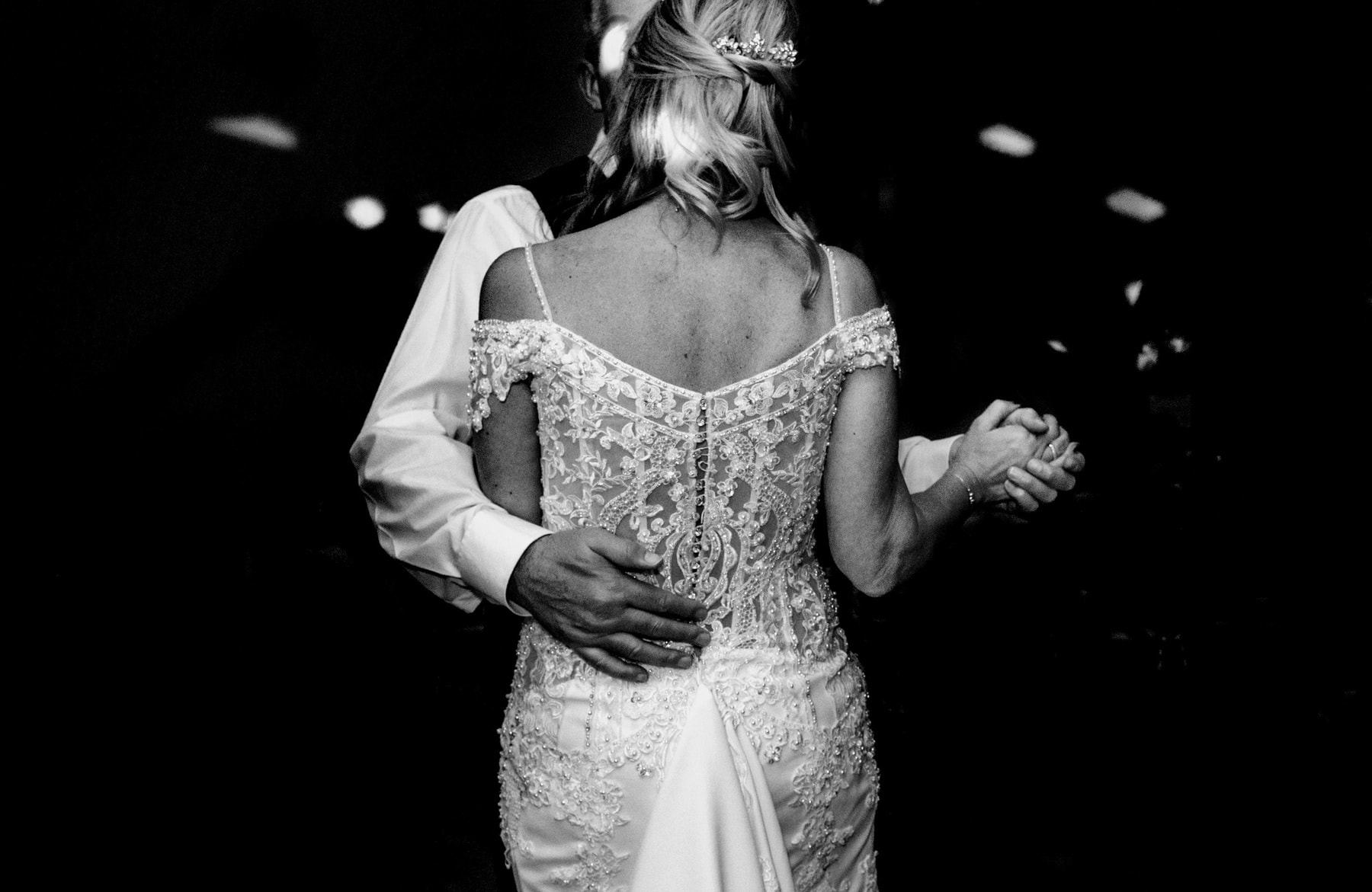 Black and white image of bride and groom having their first dance. Close up details of lace on the back of the wedding dress.
