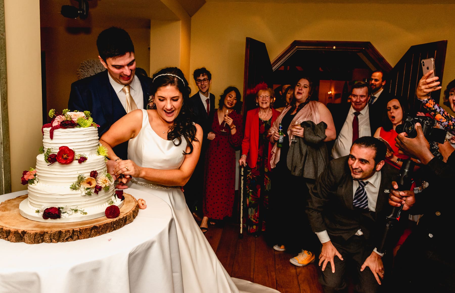 Bride and groom cut cake at a wedding with guests standing around cheering