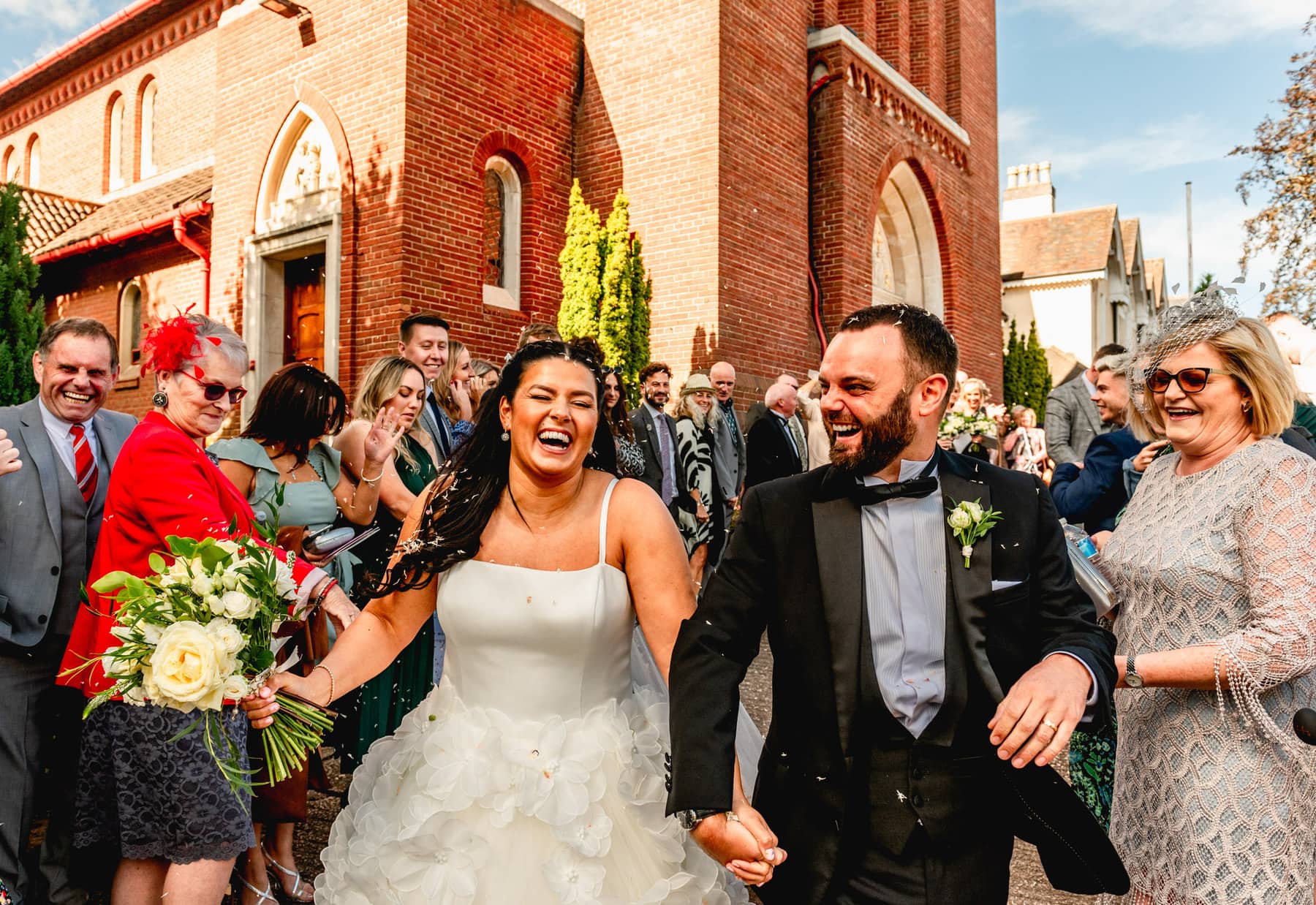 Bride and groom laugh as they run through a tunnel of confetti outside a church. Best Wedding Photography of 2021