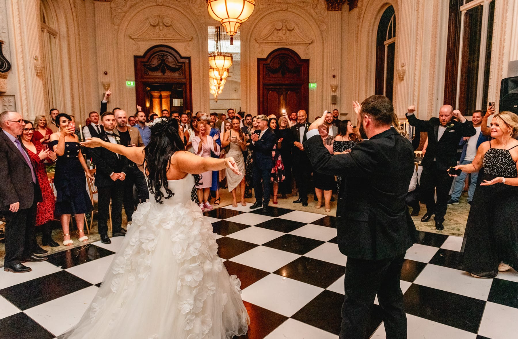 Bride and groom face the wedding guests and cheer before their first dance on a chequerboard dance floor