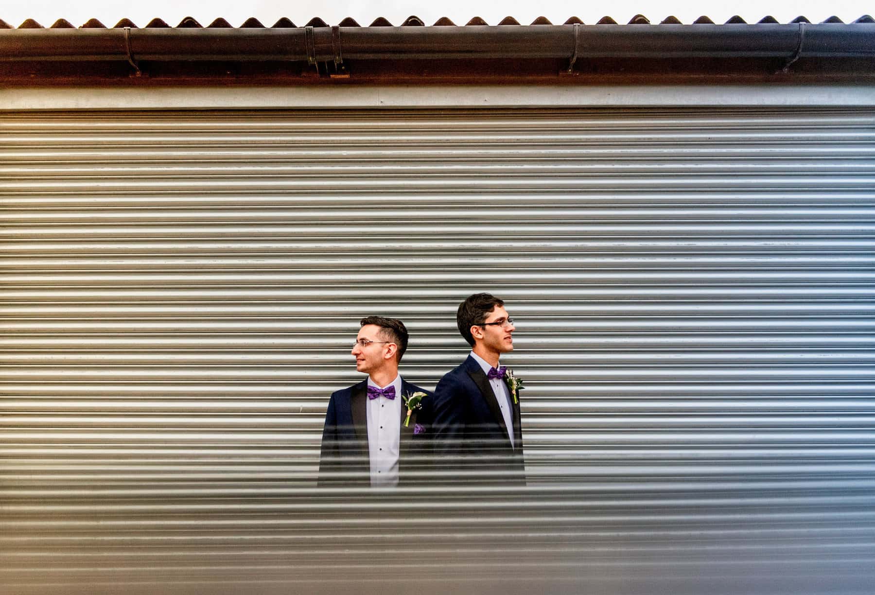Gay wedding at Mythe Barn, two men in blue dinner jackets with purple bow ties against iron background