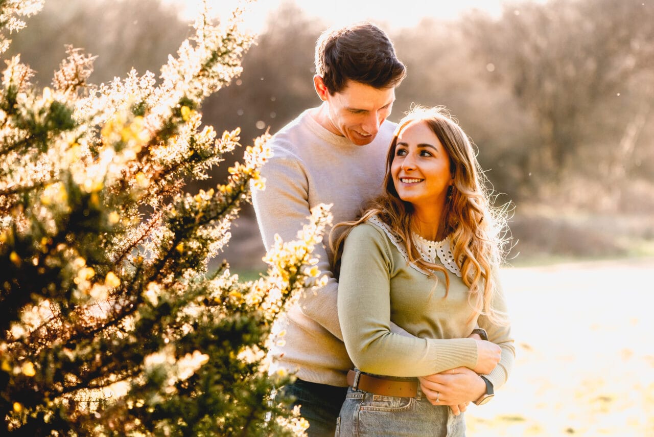 Couple cuddle on their pre wedding engagement shoot, woman wears green jumper, man wears cream