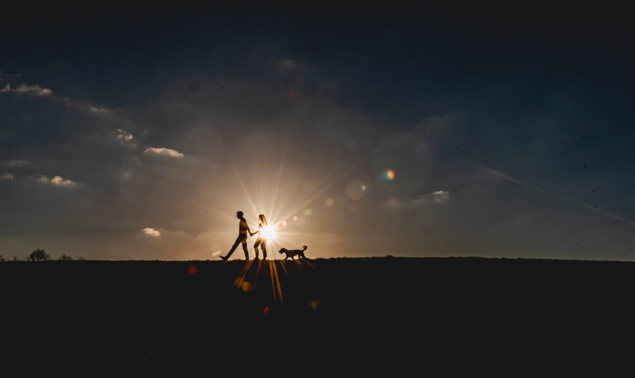 Couple and dog walking along ridge backlit by strong sun, they are silhouetted against the sun.