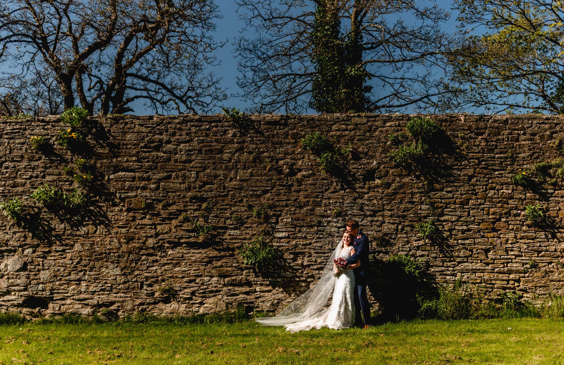 Bride and groom wedding portraits at Ludlow Castle, couple stand against surrounding walls in direct sunlight
