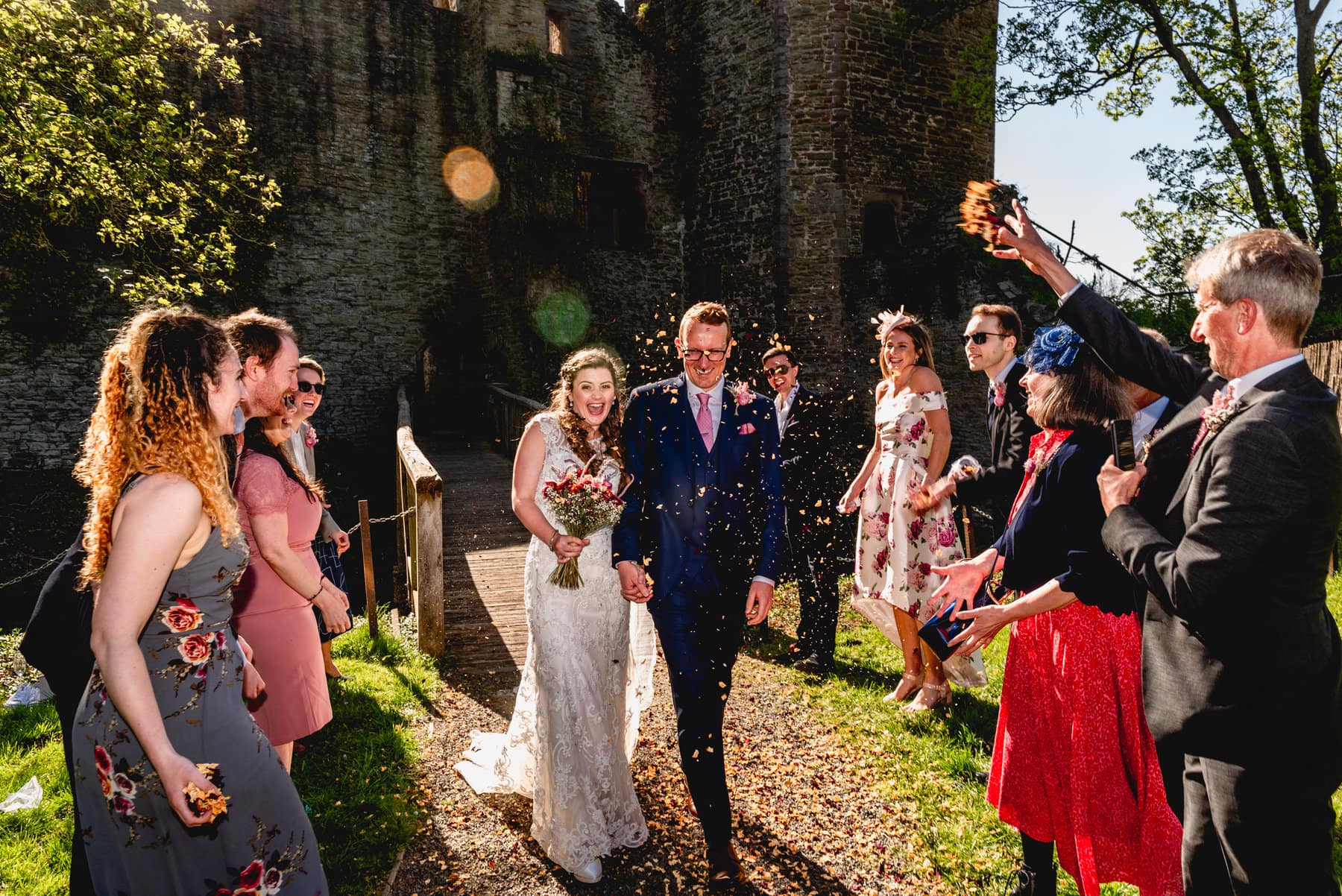 Bride and groom walk through a storm of colourful confetti at their wedding at Ludlow Castle