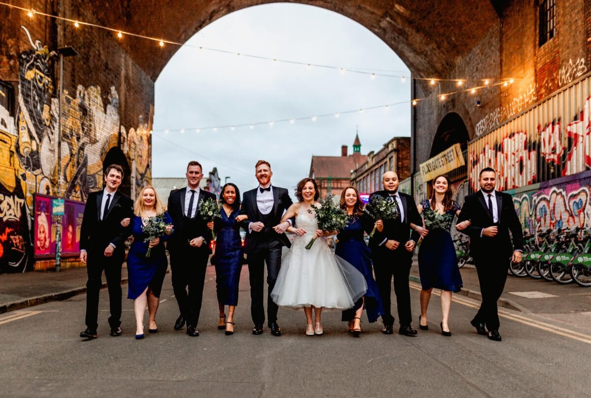 Bridal party in formal wear walk down a Digbeth Street for an urban portrait at golden hour.
