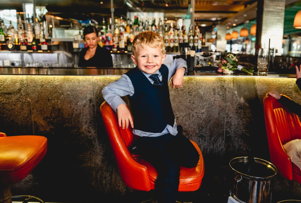 Young boy sits at a bar at The Bank Restaurant in Birmingham grinning in his suit