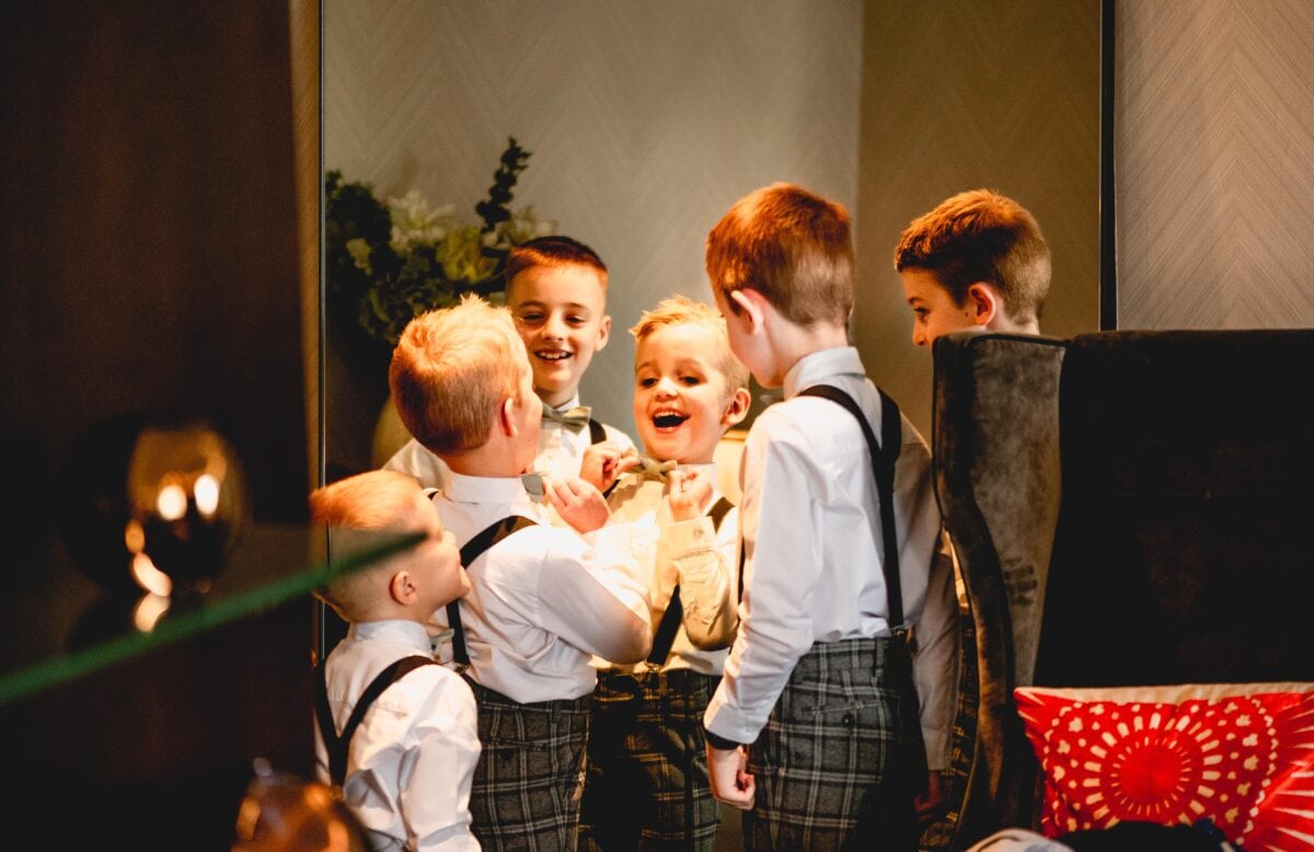 Page boys all look in a mirror while trying to do up their bowties before a wedding in Birmingham