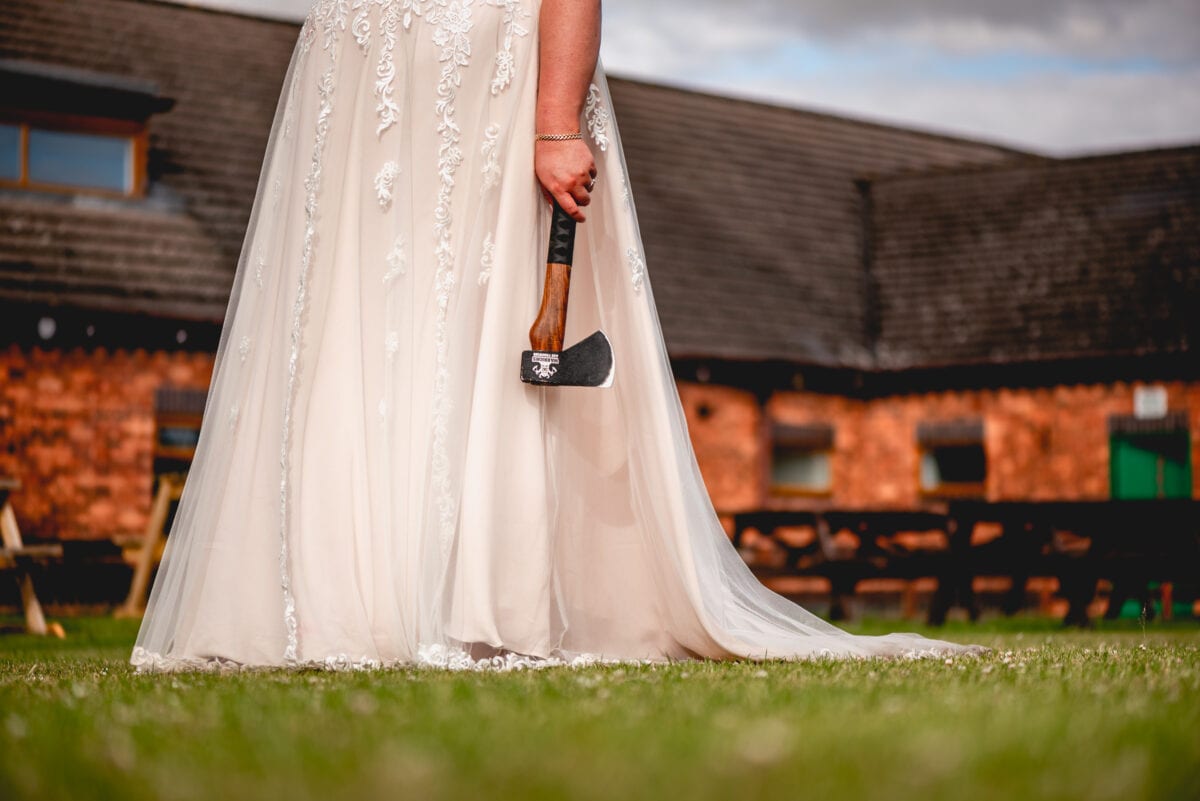 Bottom half of a bride is shown holding her axe in her wedding dress