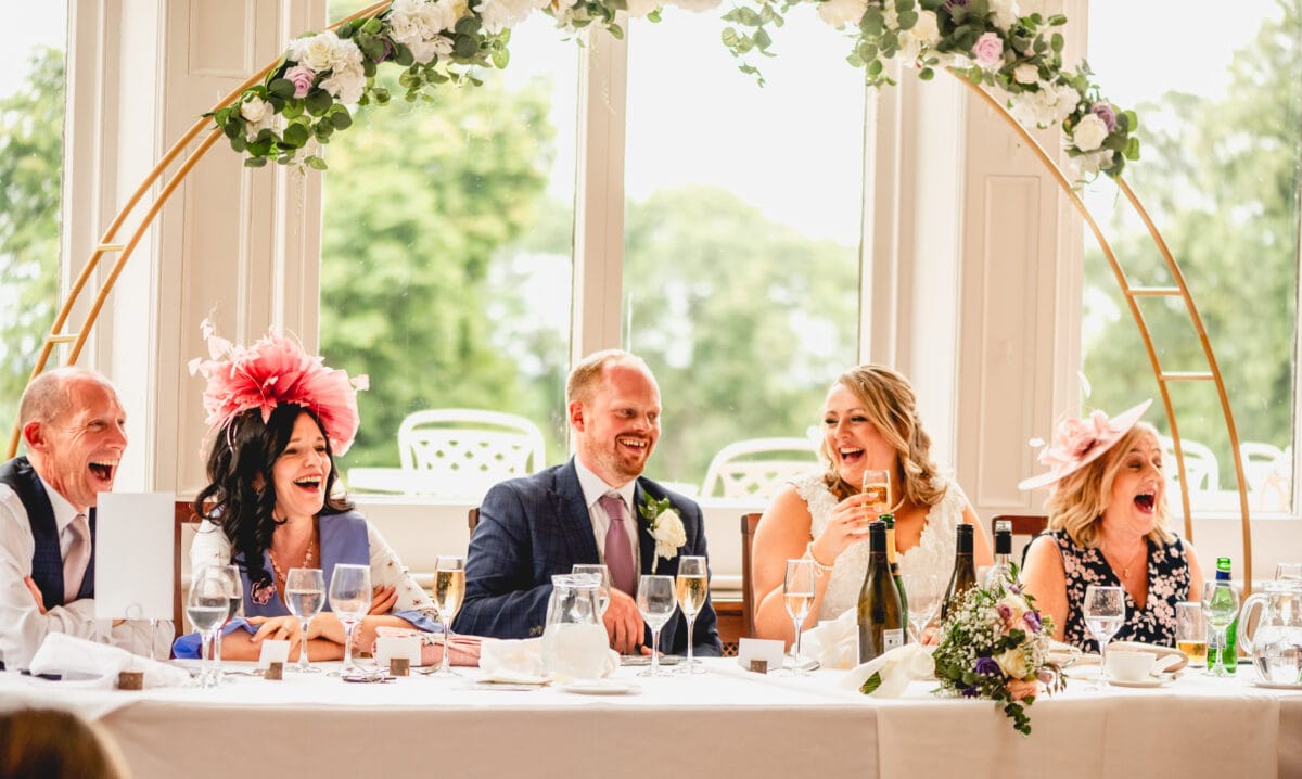 Couple and their families laugh during the speeches at their summer wedding at Pendrell Hall