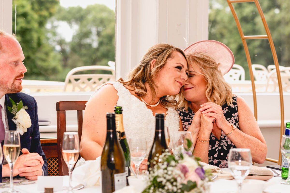 Bride and her Mom cuddle together during the speeches at couples wedding at Pendrell Hall