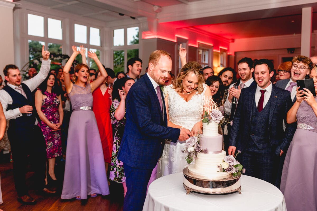 Cake cutting ceremony at a wedding reception, bride and groom are surrounded by cheering guests