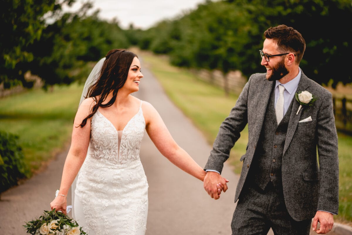Bride and groom walk towards camera smiling at each other at Mythe Barn Wedding Venue