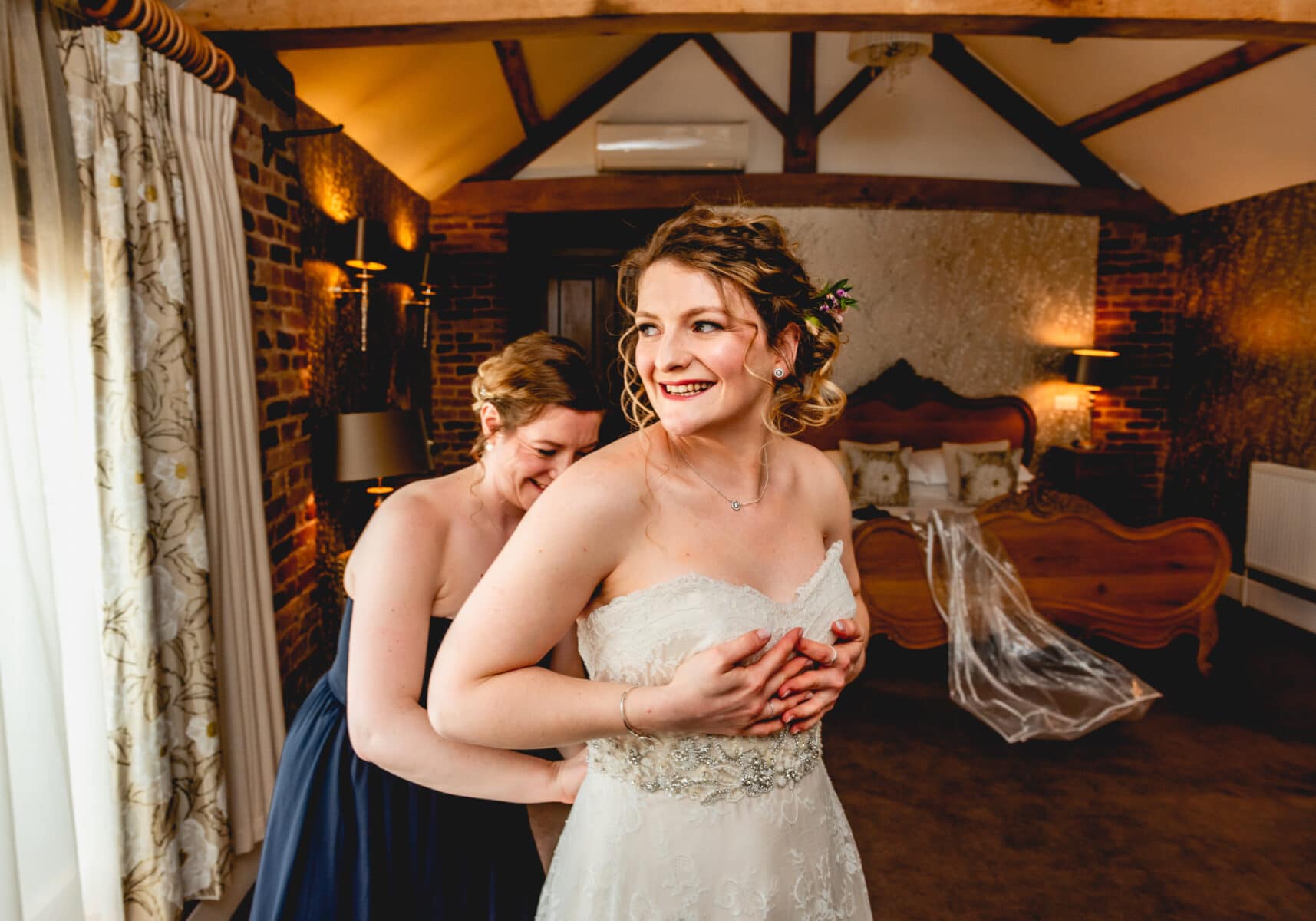 Bride is helped into her wedding dress by a bridesmaid in the bridal suite of Mythe Barn Wedding Venue