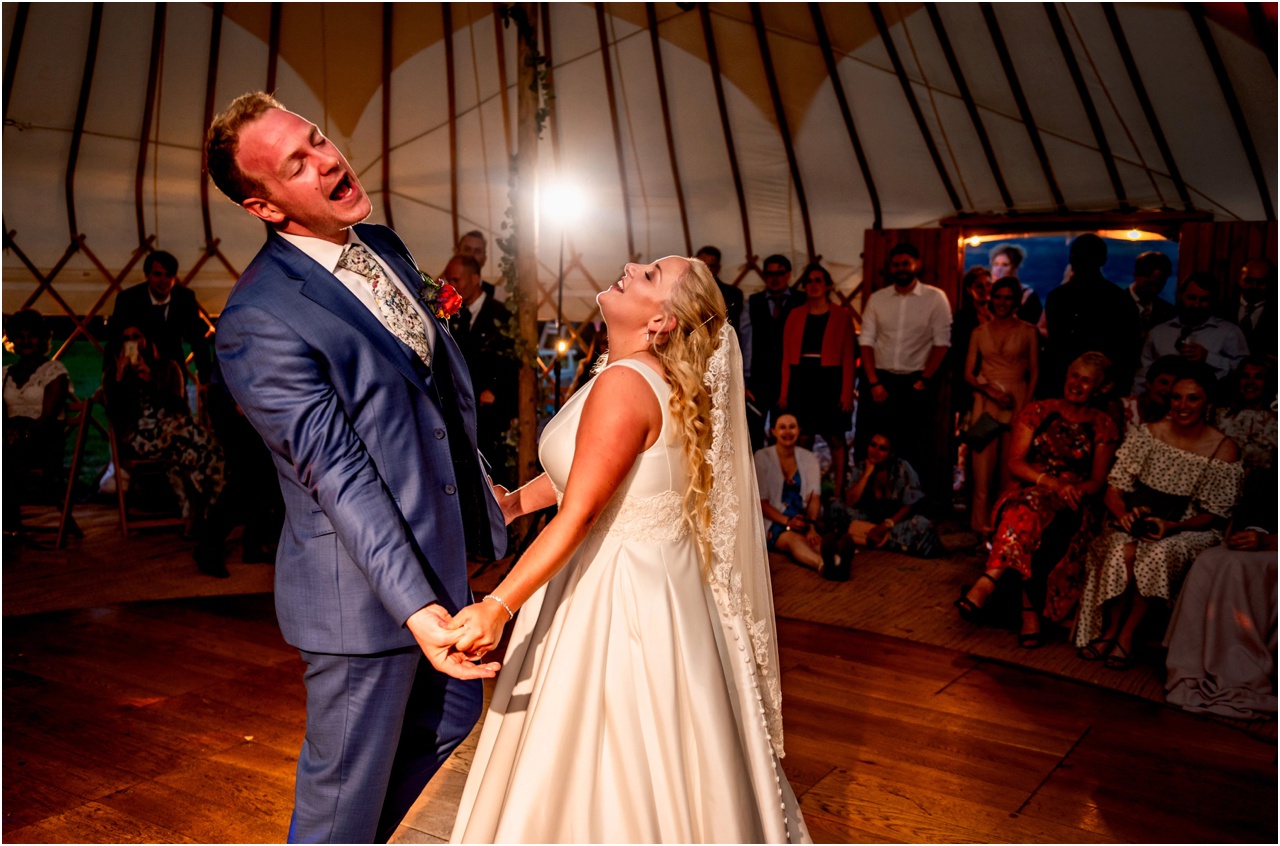 Bride and groom dance and sing out loud at their wedding first dance in a bell tent, they hold hands and throw their heads back with joy