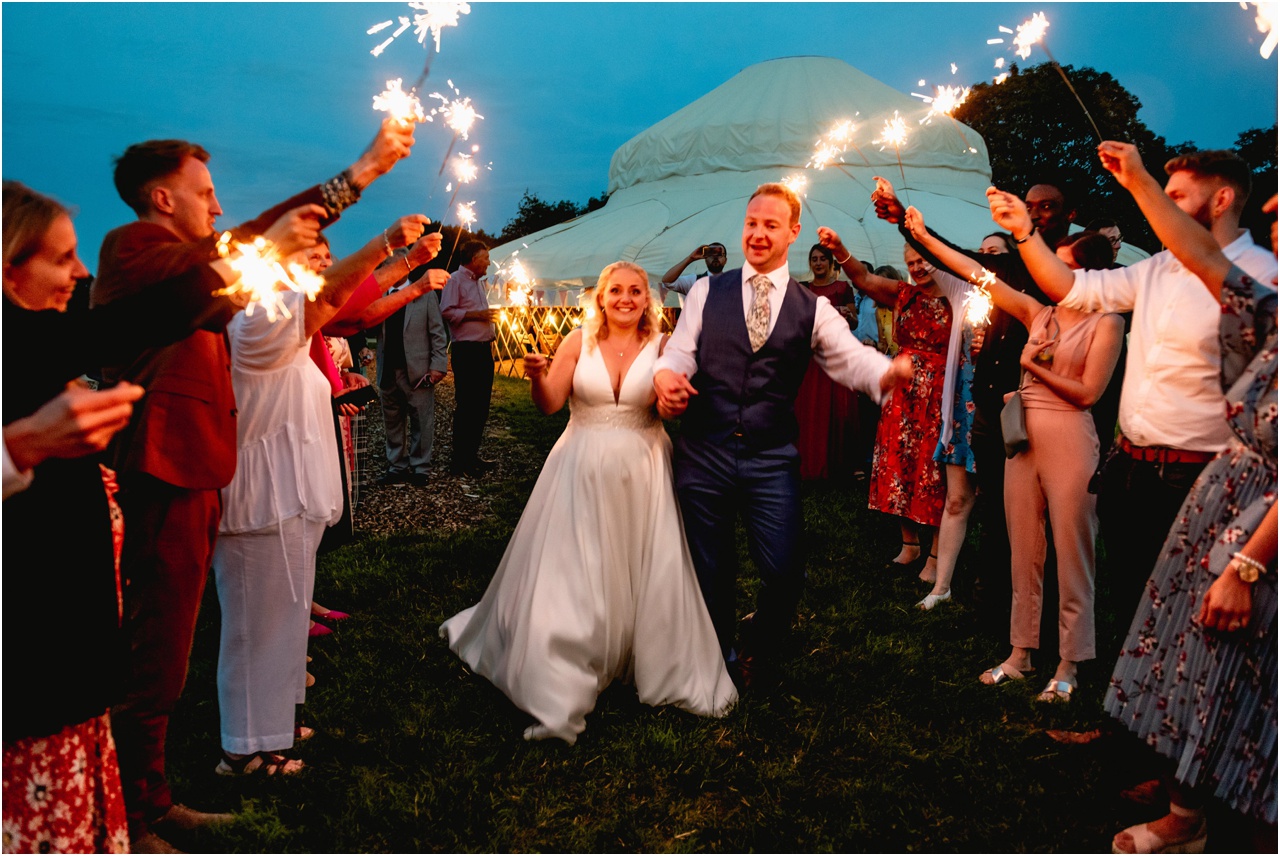 Bride and groom walk through a tunnel of sparklers at the end of their wedding in Glastonbury