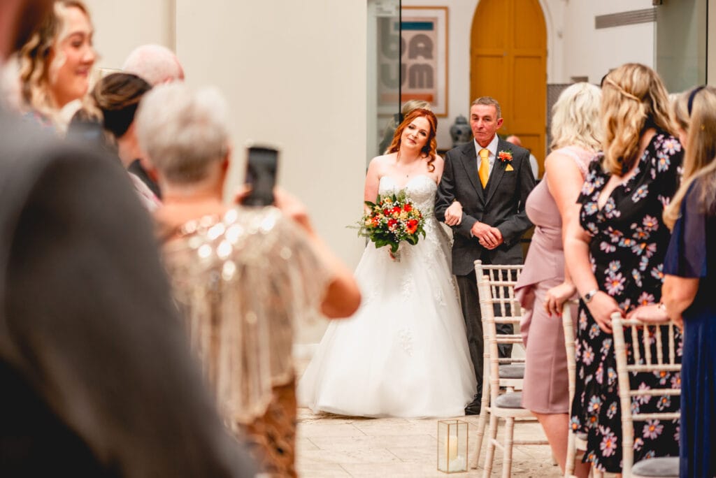 Bride is walked down the aisle by her father as guests look on
