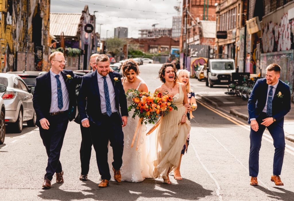 Bridal party laugh and bump into each other on an urban street in Digbeth