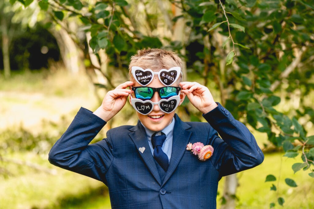 Page boy wears three pairs of novelty heart shaped wedding sunglasses