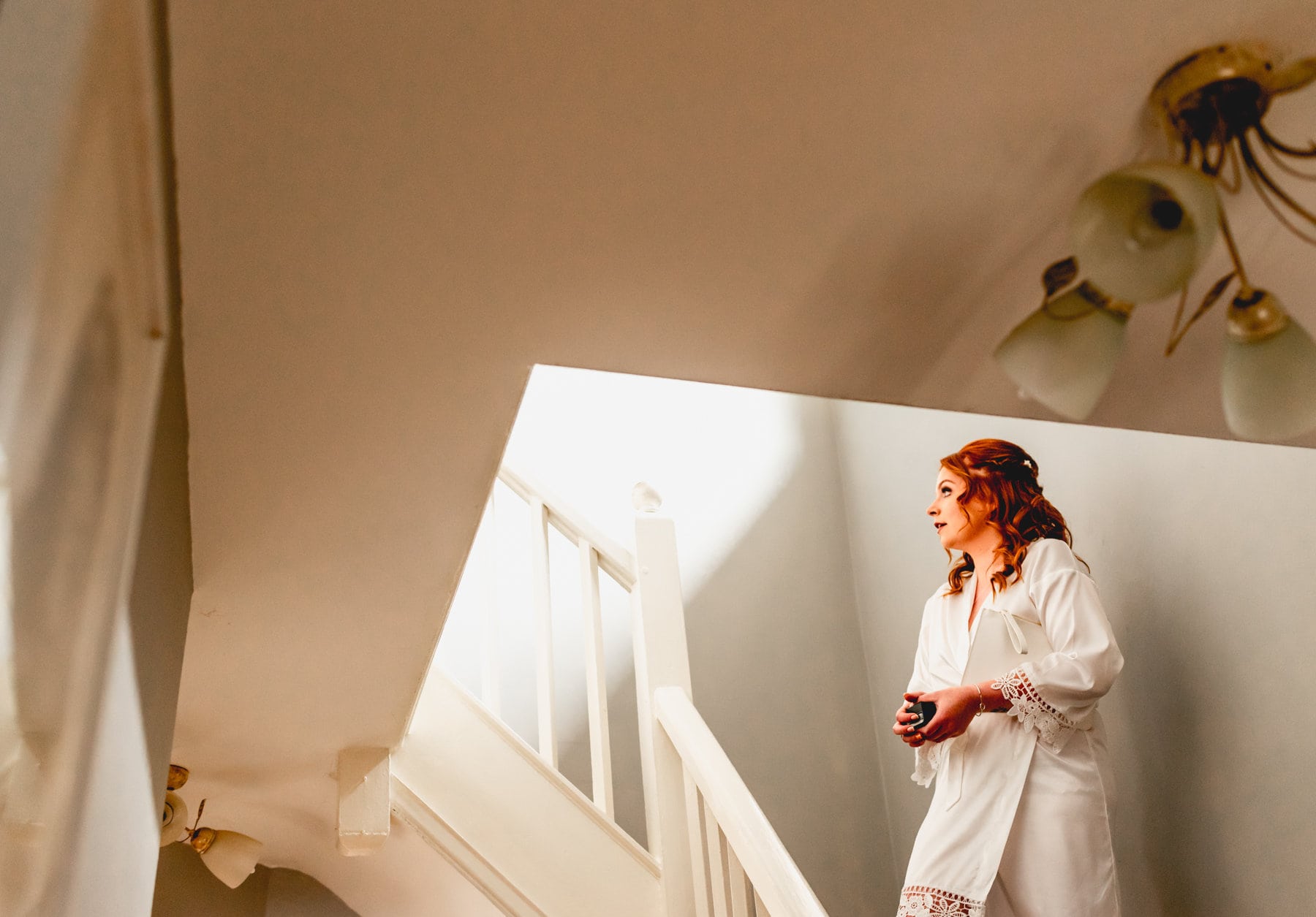 Bride waits on stairs before putting on her wedding dress. She wears a white dressing gown