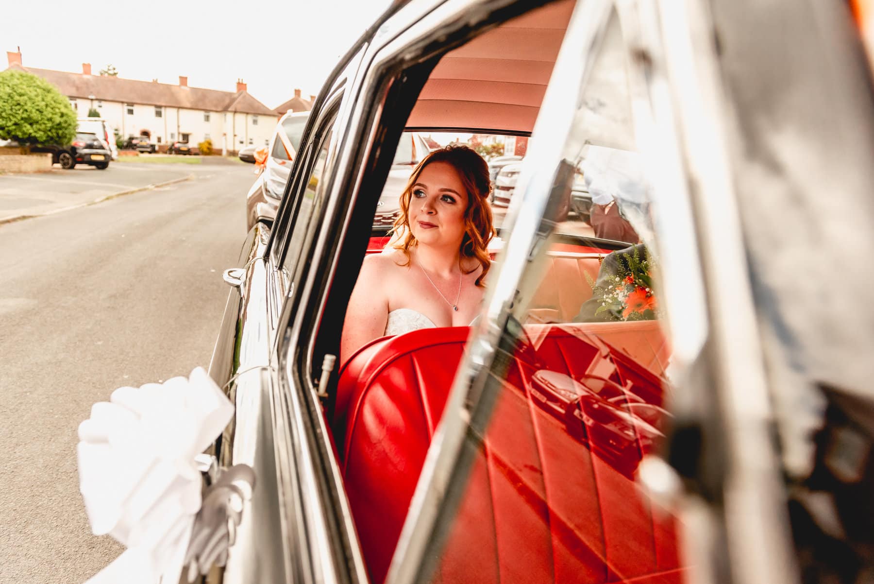 Bride in the back of her 1950's wedding car with red leather seats