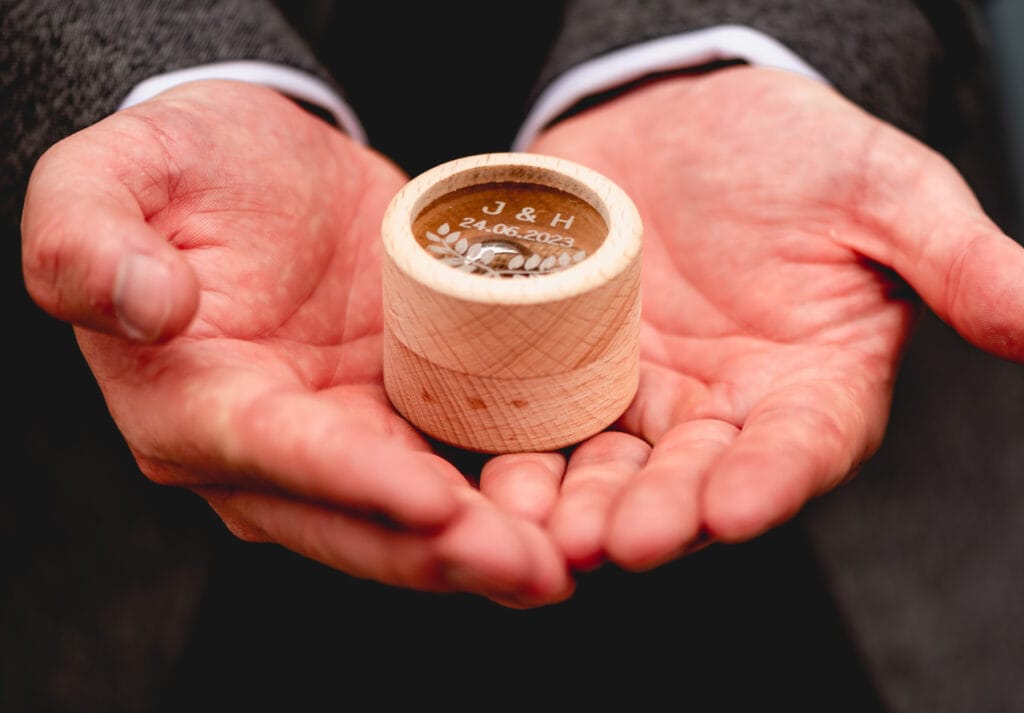 Wedding rings being held by best man in small circular wedding ring box personalised with the bride and grooms names