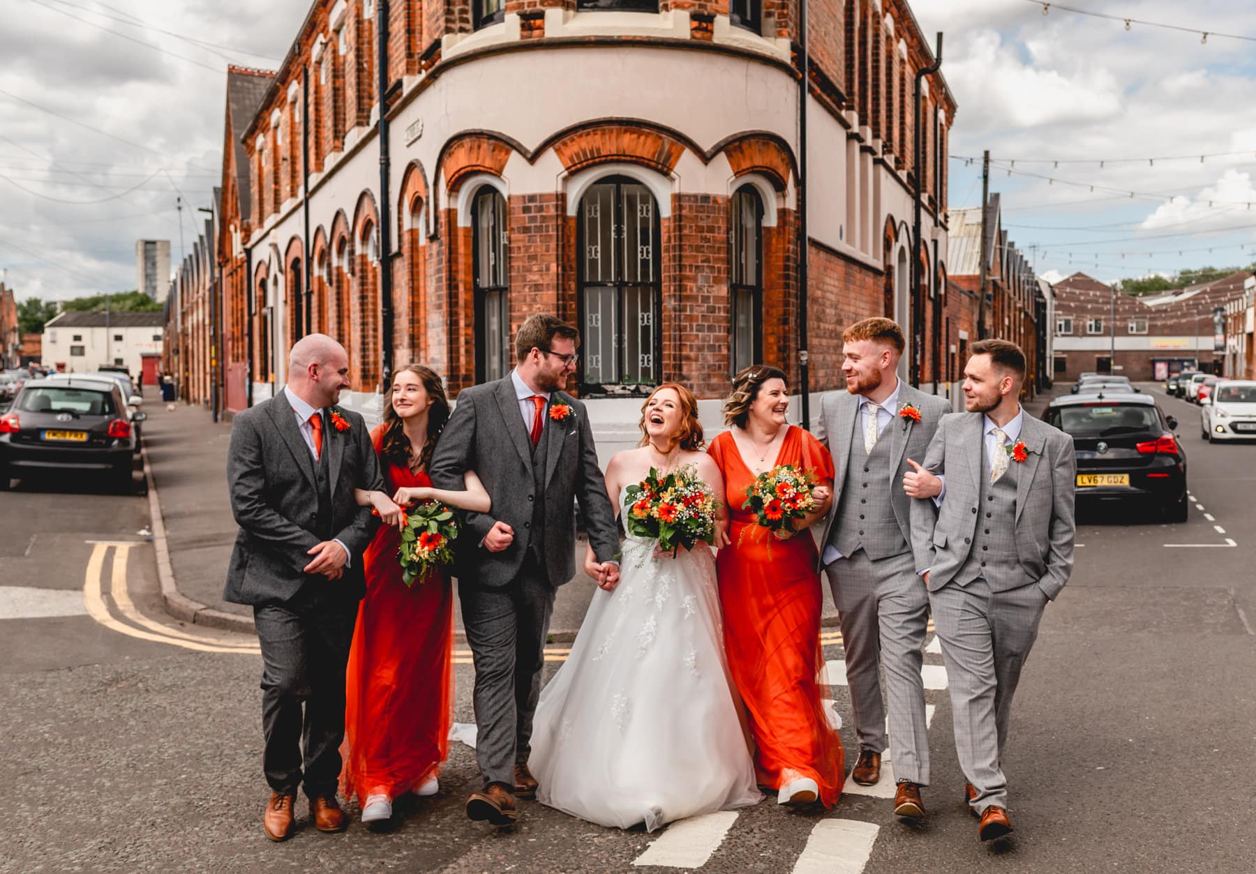 Bridal party in Digbeth, bridesmaids wear bright orange dresses, groomsmen wear grey suits with orange ties