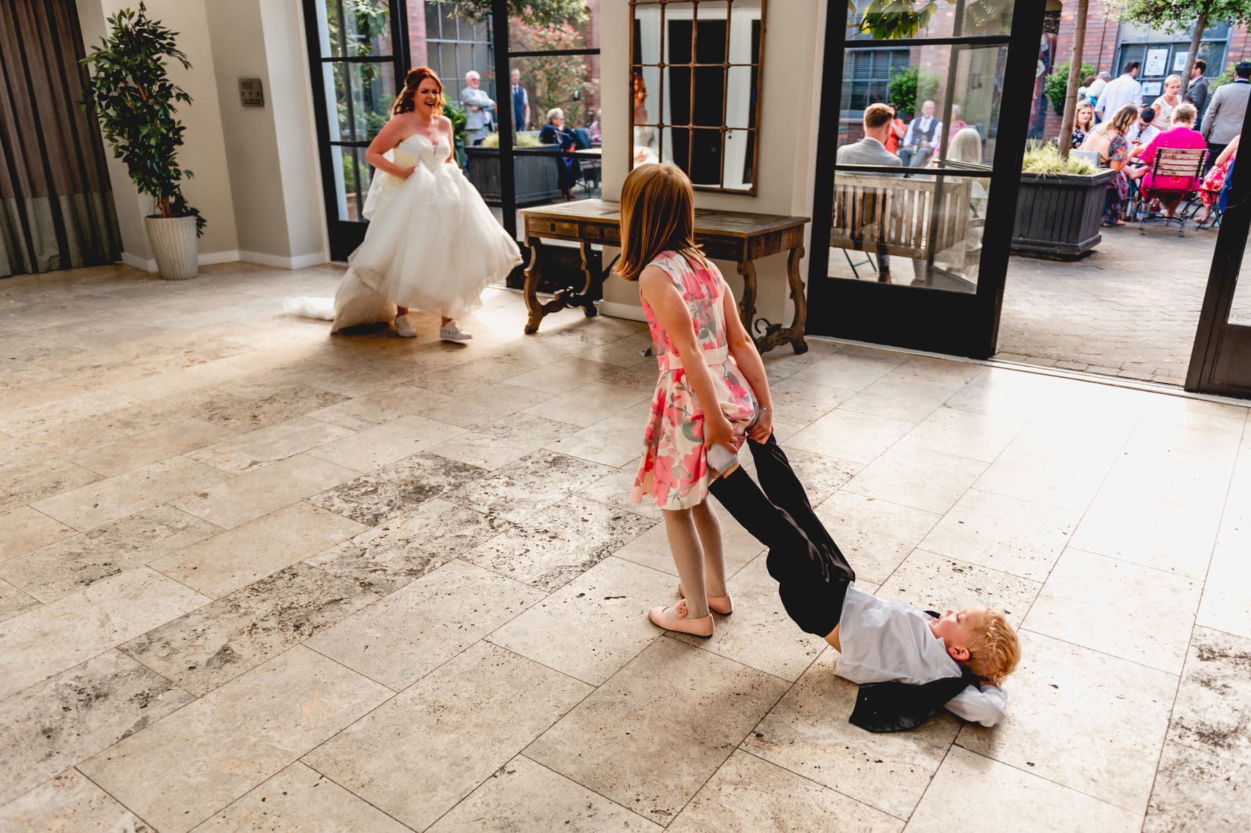 Bride laughs as flower girl pulls pageboy around the dancefloor by his feet.