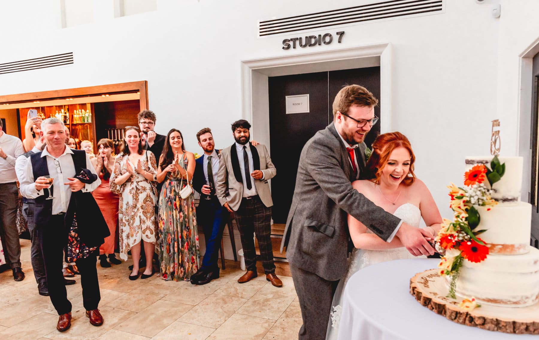 Couple cut wedding cake with guests cheering