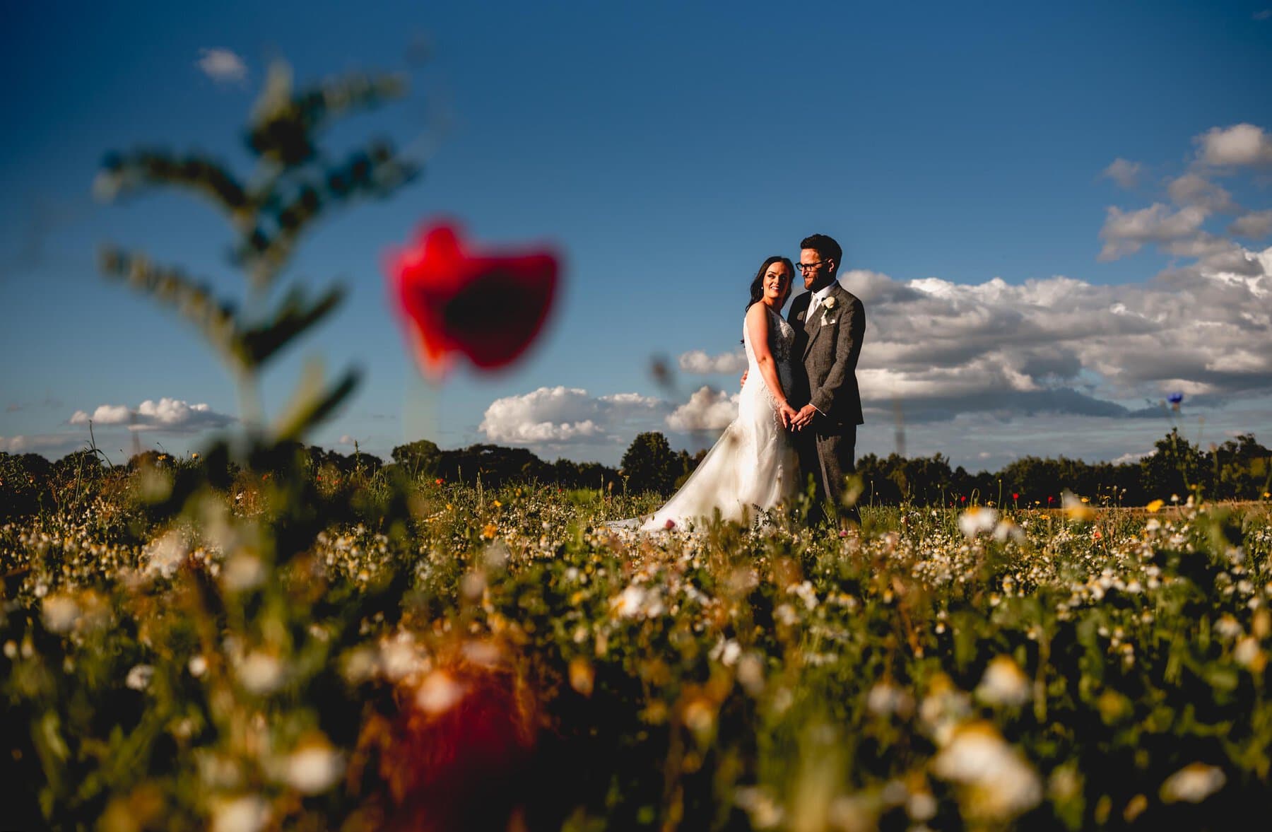 Poppy field at Mythe Barn in Atherstone, bride and groom stand in field