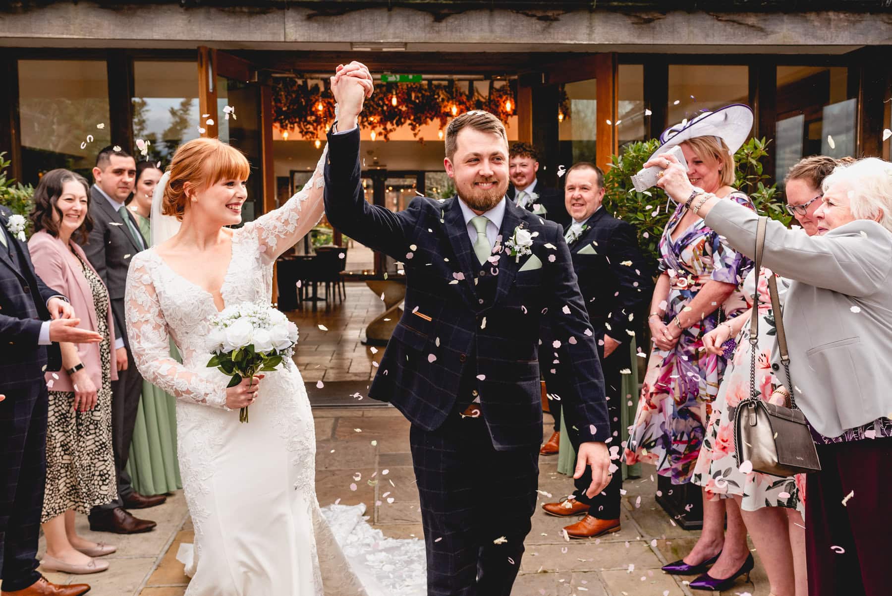 Bride and groom hold their hands aloft to celebrate as they walk through a tunnel of confetti at Mythe Barn Wedding Venue