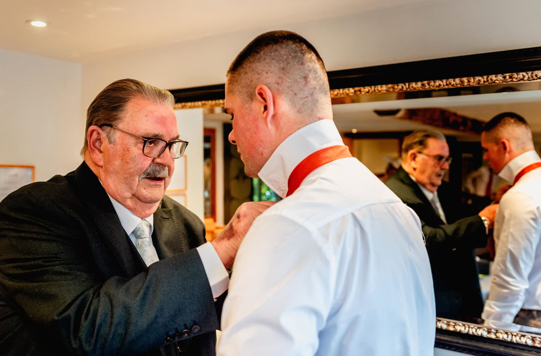 groom has help from his grandad with his orange tie on morning of wedding at Mythe Barn