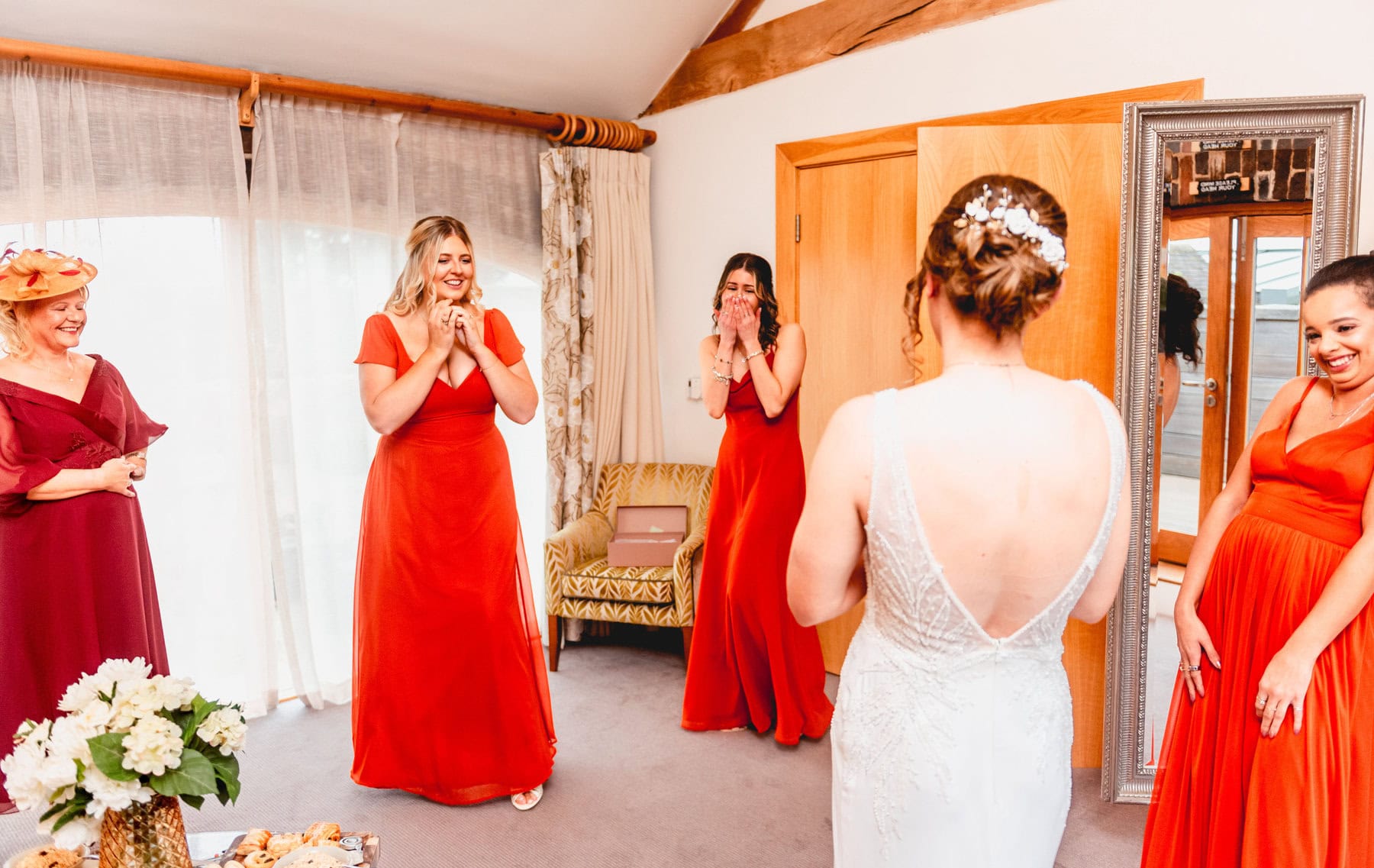 bridesmaids in orange dresses gasp as bride walks in to room on wedding morning in bridal suite 