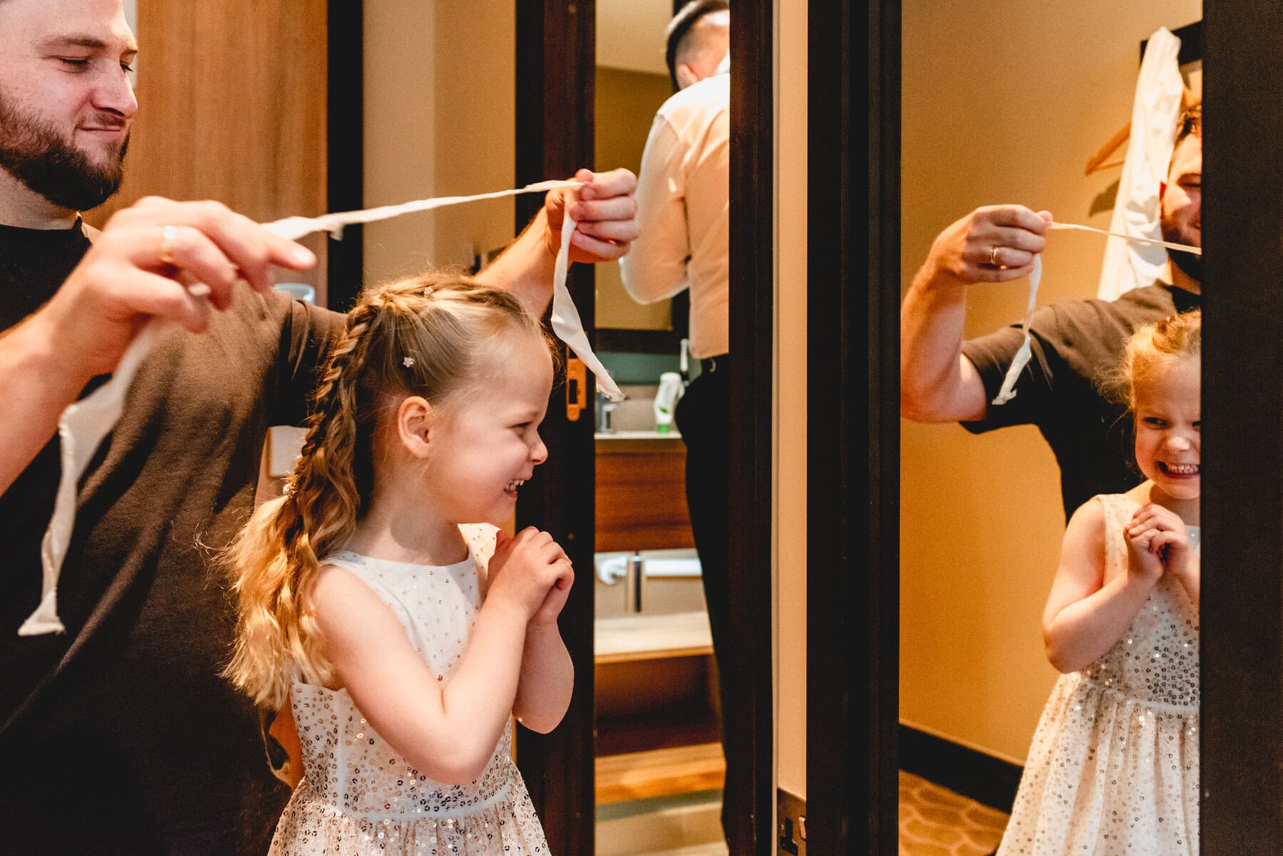 Little flower girl looks in mirror in delight as her hair is tied up before a wedding at Swallows Nest Barn